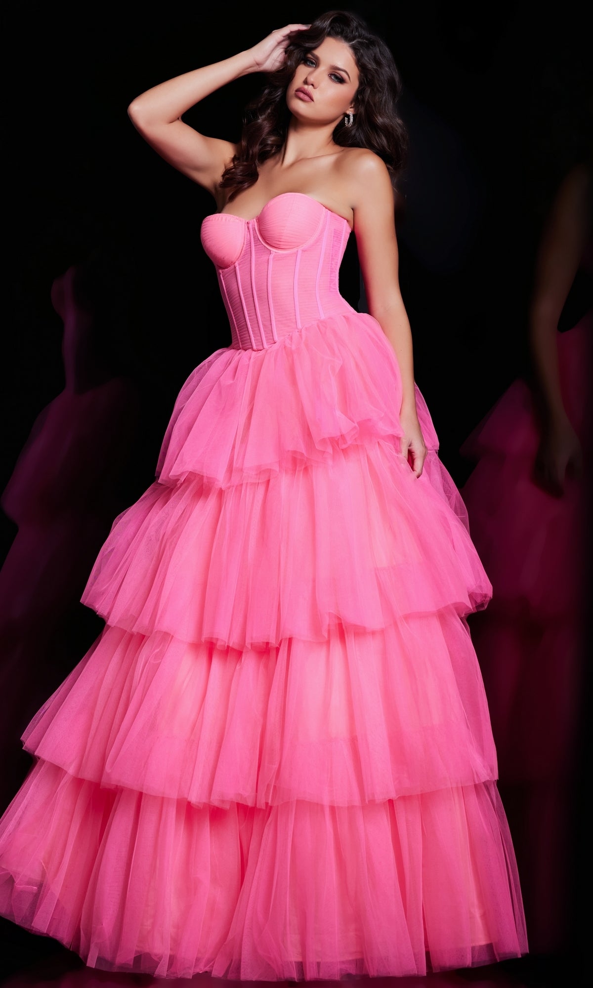 A woman stands against a black background wearing the Jovani 37062 Strapless Long Ruffle Prom Ball Gown in hot pink, featuring tiered tulle and a corset-style bodice.